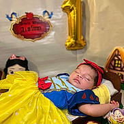 Aislinn is registered to the contest to win money with this photo: baby, sleeping, snow_white_costume, yellow_dress, red_headband, pillow, decorations, gold_balloon, number_one, bitten_apple, dwarf_figurine, fairy_tale, birthday, costume, cute, portrait, child, celebration, indoor, soft_lighting