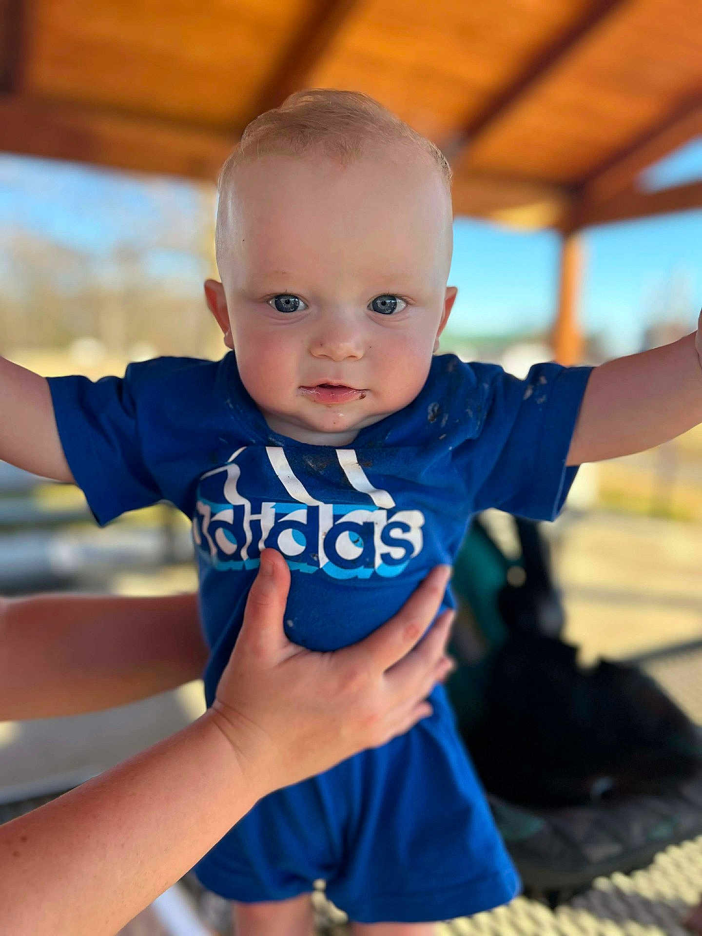 Justen is registered to the contest to win money with this photo: baby, child, blue_clothing, adidas, outdoor, daylight, hands, holding, pavilion, portrait, cute, face, smile, short_hair, person, infant, toddler, expression, skin, casual