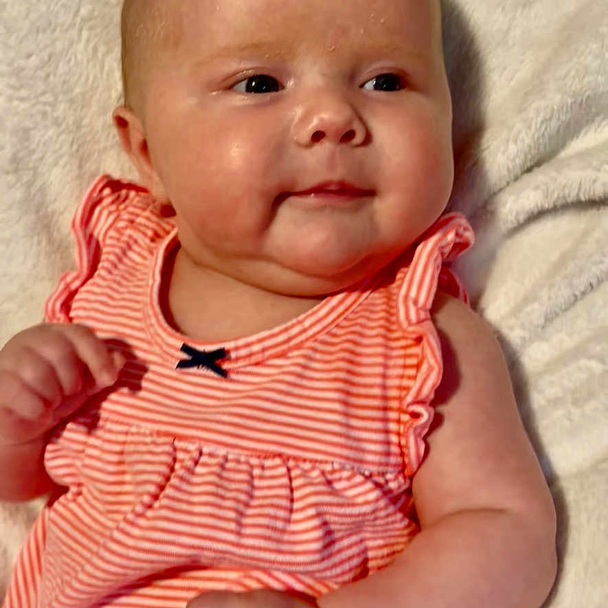 Lainey Dawn is registered to the contest to win money with this photo: baby, cheeks, child, closeup, cute, dress, fluffy, hand, happy, healthy, indoors, infant, pink, portrait, resting, smile, soft_texture, striped_clothing, white_blanket, young