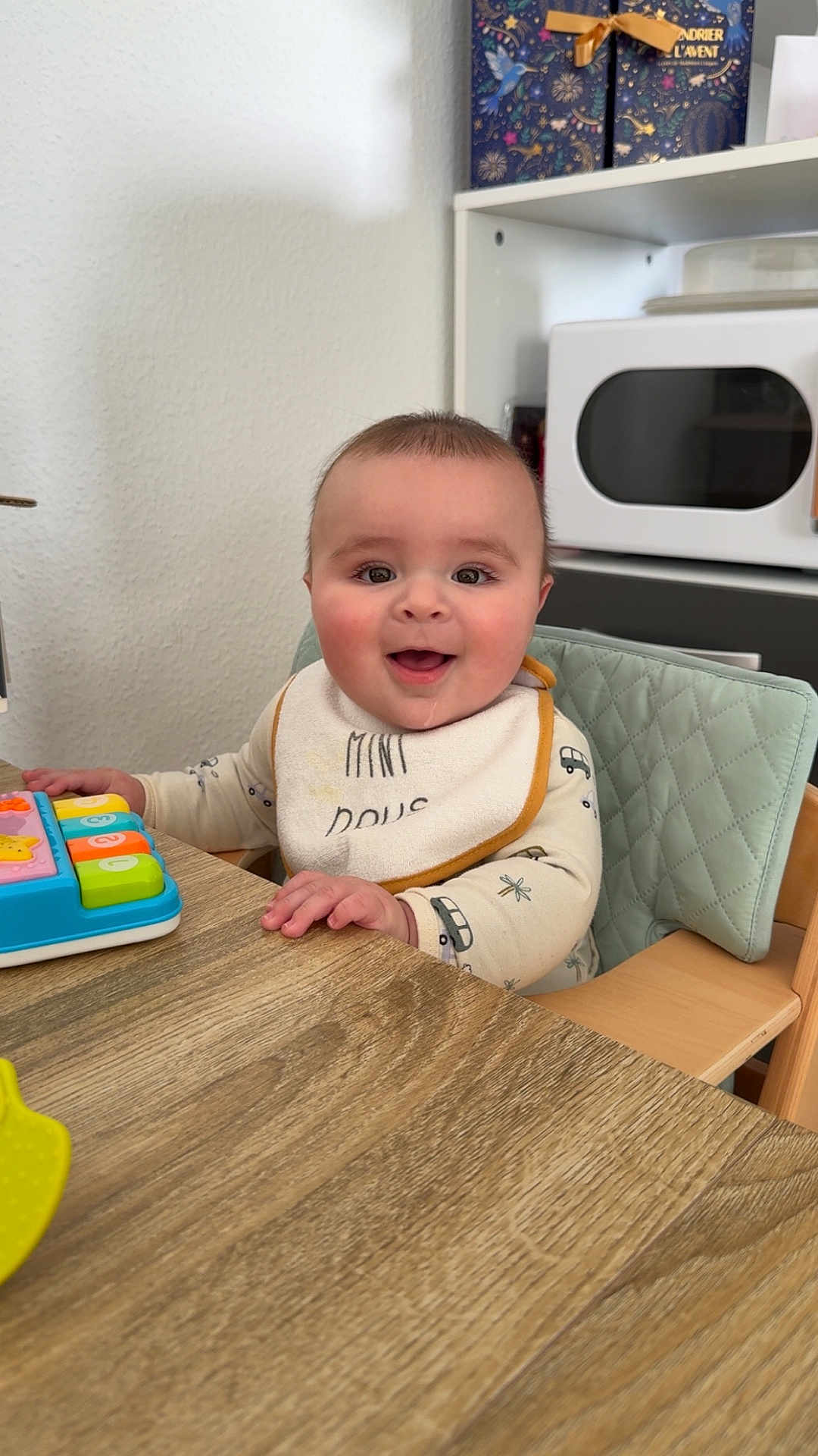 Malo a rejoint le concours — aidez-le/la à gagner de superbes lots ! baby, child, high_chair, bib, toy, table, wood, smiling, happy, indoor, face, person, clothing, kitchen, furniture, playing, cute, infant, seat, expression