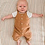 baby, infant, child, overalls, white_shirt, striped_blanket, smile, arms_outstretched, lying_down, cute, face, head, feet, skin, clothing, portrait, young_child, indoors, comfort, relaxed