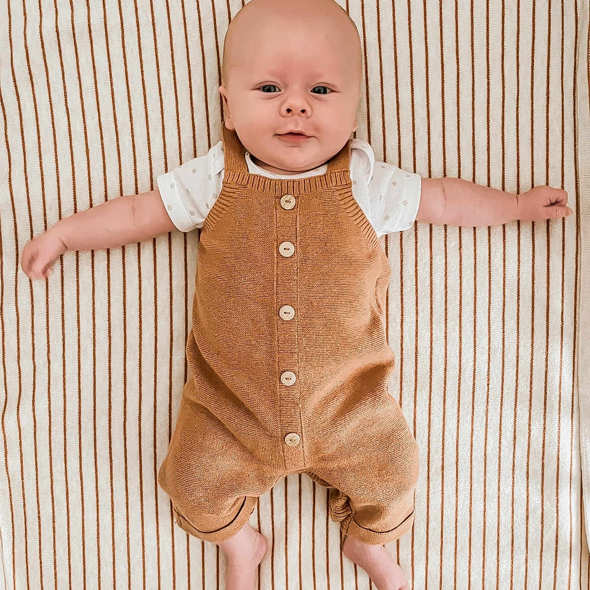 Jules a rejoint le concours — aidez-le/la à gagner de superbes lots ! arms_outstretched, baby, child, clothing, comfort, cute, face, feet, head, indoors, infant, lying_down, overalls, portrait, relaxed, skin, smile, striped_blanket, white_shirt, young_child