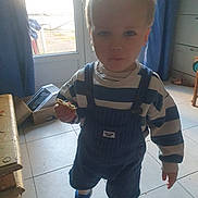 Timéo a rejoint le concours — aidez-le/la à gagner de superbes lots ! child, toddler, indoor, cookie, striped_clothing, overalls, blue_shoes, door, sunlight, curtain, tile_floor, furniture, box, window, person, young_child, standing, holding, casual_clothing, home
