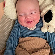 Eden is registered to the contest to win money with this photo: baby, smiling, blanket, plush_toy, blue_onesie, couch, happy, infant, cute, cozy, child, soft, sleepy, cuddly, portrait, indoor, face, hand, comfort, rest