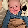 baby, smiling, blanket, plush_toy, blue_onesie, couch, happy, infant, cute, cozy, child, soft, sleepy, cuddly, portrait, indoor, face, hand, comfort, rest