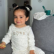 Cyana a rejoint le concours — aidez-le/la à gagner de superbes lots ! child, girl, smiling, pajamas, white_clothing, couch, indoor, home, hair_buns, snack, cozy, family_photos, wall_art, relaxed, seated, cute, young_child, portrait, living_room, comfort