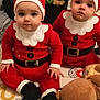 babies, baby, black_boots, child, christmas_costume, cute, expression, face, festive, floor_mat, holiday, indoor, infant, person, plush_toy, red_clothing, santa_hat, sitting, toy, white_trim