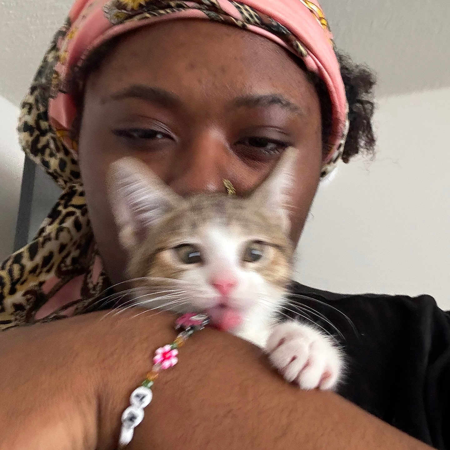 Xylon is registered to the contest to win money with this photo: affection, animal, arm, black_shirt, bracelet, brown_skin, cat, closeup, cute, expression, face, fur, hand, headscarf, holding, indoor, kitten, licking, person, pet