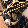 cat, gray_tabby, laundry_basket, clothes, hanger, indoor, carpet, bag, pile, fabric, curious, pet, domestic_animal, yellow_eyes, looking_up, room, storage, casual, household, cozy