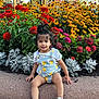 toddler, child, flower_bed, flowers, outdoor, plants, greenery, curb, sidewalk, romper, sneakers, hair_tied_up, yellow_flowers, red_flowers, pink_flowers, white_flowers, daylight, nature, casual_clothing, garden