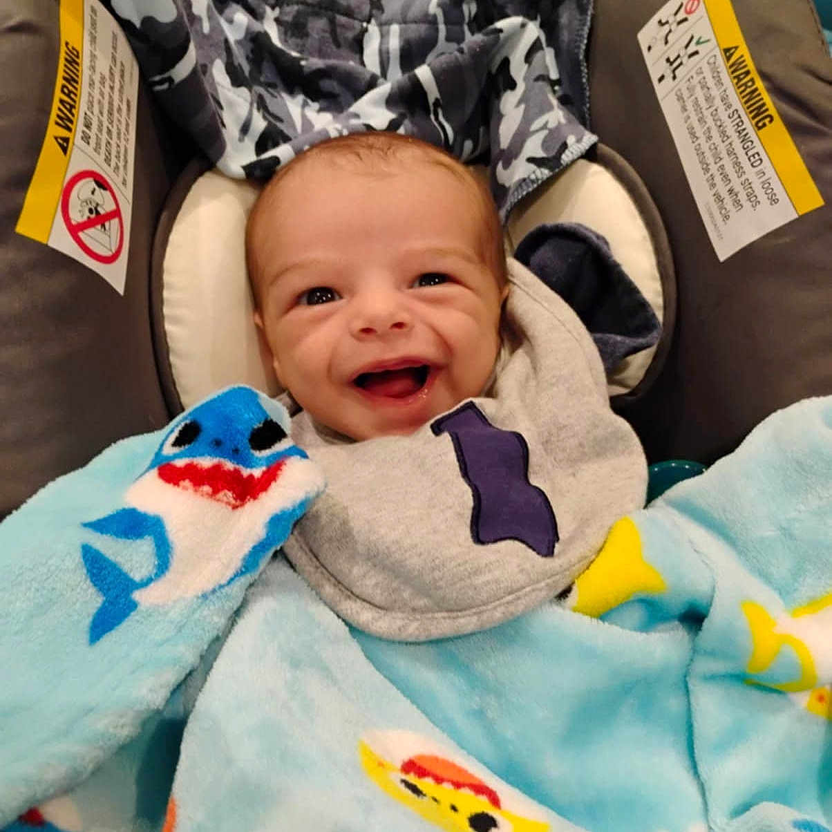 Niyel is registered to the contest to win money with this photo: baby, blanket, blue_blanket, camo_fabric, car_seat, child, clothing, comfort, cozy, cute, face, fish_pattern, happy, head, indoor, infant, portrait, seat, smiling, young