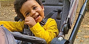 Ky-Mani a rejoint le concours — aidez-le/la à gagner de superbes lots ! toddler, child, stroller, yellow_shirt, smiling, happy, outdoor, park, playground, trees, daylight, curly_hair, seatbelt, casual_clothing, baby_walker, nature, baby, seat, play_area, joyful