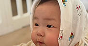 Rocky is registered to the contest to win money with this photo: baby, child, infant, hood, cute, face, cheeks, soft, lying_down, indoor, curious, white, colorful_prints, background_blur, crib, clothing, person, portrait, closeup, young