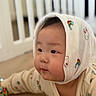 baby, child, infant, hood, cute, face, cheeks, soft, lying_down, indoor, curious, white, colorful_prints, background_blur, crib, clothing, person, portrait, closeup, young