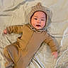baby, infant, onesie, knitted_hood, blanket, lying_down, cute, smiling, child, portrait, indoors, soft_lighting, warm_colors, cozy, person, young_child, sleepwear, baby_clothes, happy, face