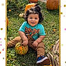 child, toddler, pumpkins, grass, outdoor, scooby_doo, gourd, curly_hair, smiling, fall, autumn, casual_clothing, blue_shoes, greenery, playful, cute, festive, nature, happy, sitting