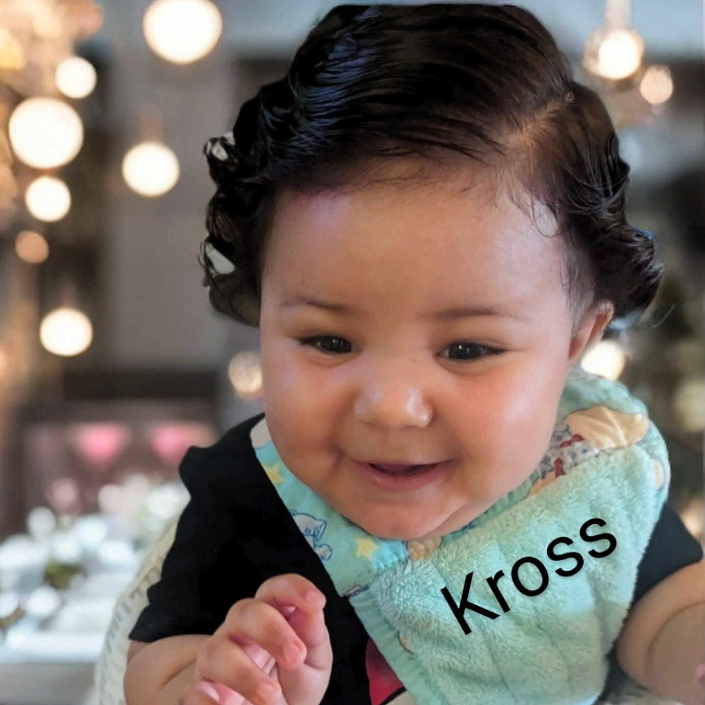 Kross is registered to the contest to win money with this photo: baby, child, smile, curly_hair, bib, clothing, face, hand, indoor, bokeh, lighting, person, cute, portrait, happy, infant, closeup, skin, young, expression