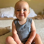 Silas is registered to the contest to win money with this photo: baby, background, bed, carpet, child, chubby_cheeks, cute, face, gray_onesie, hands, happy, indoors, infant, legs, mohawk, pillow, portrait, sitting, skin, smile