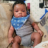 Michael is registered to the contest to win money with this photo: arms, baby, bib, blue_bib, child, clothing, cushion, cute, expression, face, gray_onesie, hand, indoor, infant, legs, patchwork, quilt, relaxed, sock, sofa