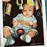 Banx joined the competition — help win amazing prizes! baby, car_seat, child, clothing, colorful, face, handwritten_date, head, indoor, infant, person, photograph, polaroid, portrait, romper, seat_belt, serious_expression, socks, toy, warning_label