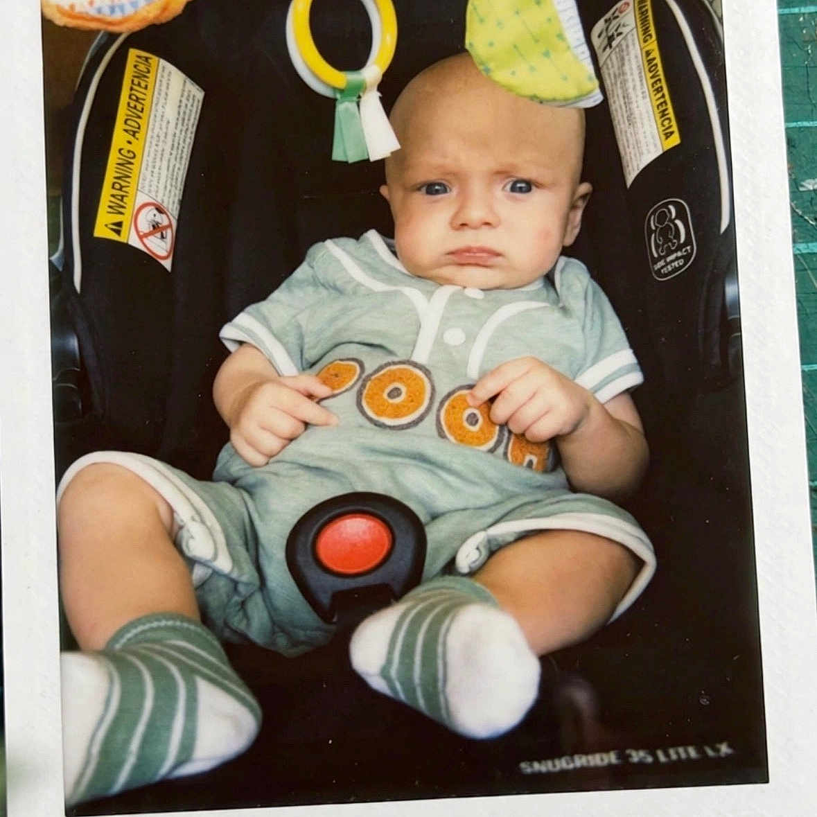 Banx joined the competition — help win amazing prizes! baby, car_seat, child, clothing, colorful, face, handwritten_date, head, indoor, infant, person, photograph, polaroid, portrait, romper, seat_belt, serious_expression, socks, toy, warning_label