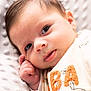 baby, infant, close_up, face, hand, eyes, blanket, soft_texture, clothing, embroidered_letters, dog_illustration, cute, resting, portrait, newborn, skin, young_child, indoors, warm, comfort