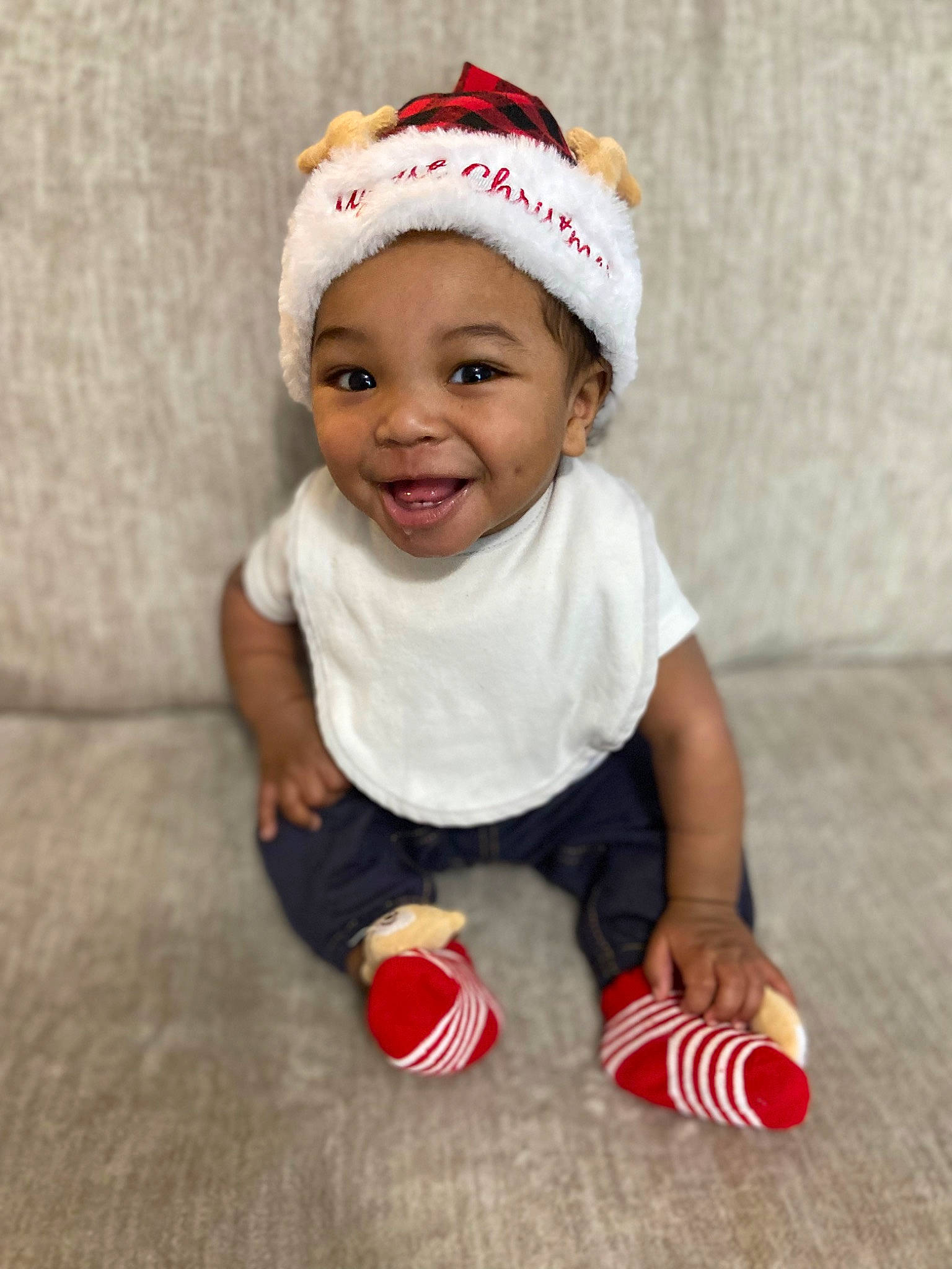 Elijah is registered to the contest to win money with this photo: baby, baby_toddler_clothing, cap, child, face, fashion_accessory, flooring, foot, happy, headwear, human_leg, joy, knee, pattern, person, red, sleeve, smile, sock, t_shirt