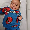 baby, child, smiling, spiderman, blue_clothing, cute, infant, portrait, lying_down, happy, person, face, hand, indoors, soft_surface, casual_wear, young_child, playful, cartoon_character, toddler