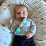 baby, infant, toy, pillow, sheep_pattern, clothing, grey_shirt, navy_pants, hand, face, expression, lying_down, cute, indoor, child, young_child, person, comfort, playful, soft