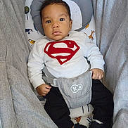 Liam participe au concours pour gagner de l'argent avec cette photo : baby, black_pants, child, clothing, comfortable, cushion, cute, footwear, gray, indoor, infant, looking_at_camera, portrait, red, seat, sneakers, superman_logo, sweatshirt, white, young_child
