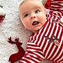 baby, infant, red_striped_clothing, christmas_ornaments, plush_reindeer, white_blanket, holiday, festive, blue_eyes, cute, portrait, smiling, child, soft_texture, cozy, seasonal, celebration, decoration, holiday_outfit, lying_down