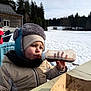 toddler, child, winter_clothing, hat, scarf, bottle, snow, outdoor, table, fries, wooden_building, forest, cold_weather, beverage, jacket, seat, daylight, nature, casual, portrait
