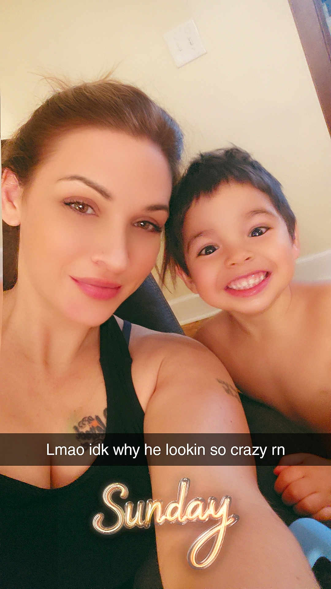 Noah is registered to the contest to win money with this photo: woman, child, smiling, selfie, face, portrait, tattoo, indoors, casual, happy, black_tank_top, short_hair, brown_hair, light_skin, cheerful, playful, caption_overlay, text_overlay, sunday, young_boy
