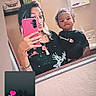 woman, child, toddler, mirror_selfie, bathroom, phone, pink_phone_case, heart_doodle, casual_clothing, reflection, shelf, framed_picture, music_overlay, comment, social_media, facial_expression, indoor, portrait, family, playful