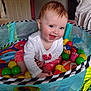 baby, child, playpen, toys, balls, smiling, happy, indoors, colorful, clothing, sitting, face, person, cute, infant, playtime, mesh, home, cheerful, young