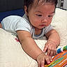 baby, infant, child, portrait, bed, bedding, indoors, bedroom, lying_down, reaching, toy, activity_book, colorful, striped_clothing, short_sleeves, dark_hair, curious, face, hands, cozy