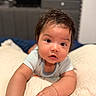 Ezekiel is registered to the contest to win money with this photo: baby, infant, child, portrait, face, wide_eyed, curious, indoor, bedroom, bed, blanket, bedding, striped_shirt, short_hair, brown_hair, sitting, crawling, hands, warm_lighting, home
