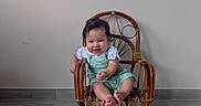Eliana joined the competition — help win amazing prizes! baby, child, smiling, green_overall, white_shirt, wooden_chair, indoor, floor, window, wall, plaque, milestone, happy, cute, portrait, toes, sitting, person, home, young