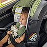 toddler, child, car_seat, pacifier, stuffed_animal, toy, green_canopy, car_interior, seatbelt, baby, cute, safety, resting, side_view, window, vehicle, infant, young_child, car_safety, bracelet