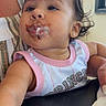 Eliana joined the competition — help win amazing prizes! baby, child, face, messy_face, chocolate, cream, pink_clothing, earrings, person, indoor, curly_hair, striped_shirt, adult_arm, table, napkin, window, highchair, portrait, cute, expression