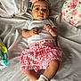baby, infant, child, headband, flower, pink, white, bed, pillow, clothing, shorts, socks, cute, lying_down, indoors, portrait, person, skin, smiling, hands