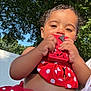 child, toddler, red_clothing, polka_dot, toy, outdoor, sunlight, trees, greenery, blue_sky, cute, face, hands, summer, playful, baby, nature, happy, skin, dress