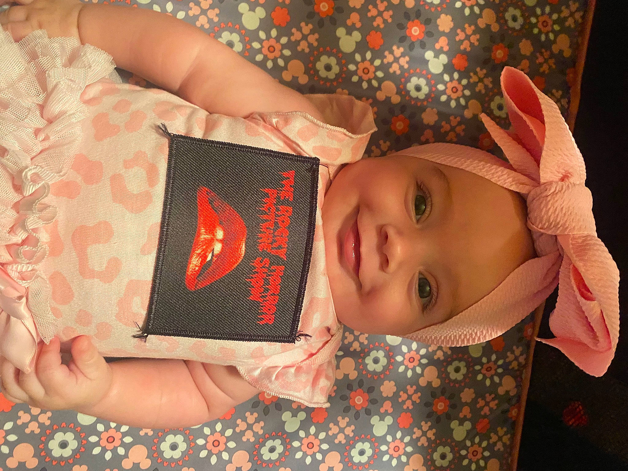 Esme is registered to the contest to win money with this photo: arm, baby, baby_toddler_clothing, cheek, child, eye, facial_expression, finger, hand, happy, head, headwear, joy, lip, nail, pattern, person, pink, skin, sleeve