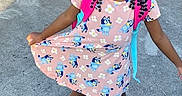 Robyn joined the competition — help win amazing prizes! child, girl, braided_hair, dress, cartoon_print, backpack, outdoor, concrete, shadow, purple_wall, metal_chair, smile, playful_pose, sunny_day, footwear, happy, young, person, standing, casual_clothing