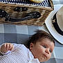 baby, infant, white_outfit, blanket, picnic_basket, bananas, grapes, dessert, candle, number_two, hat, airplane_pin, checkered_pattern, food, fruit, lying_down, curious, indoors, closeup, portrait