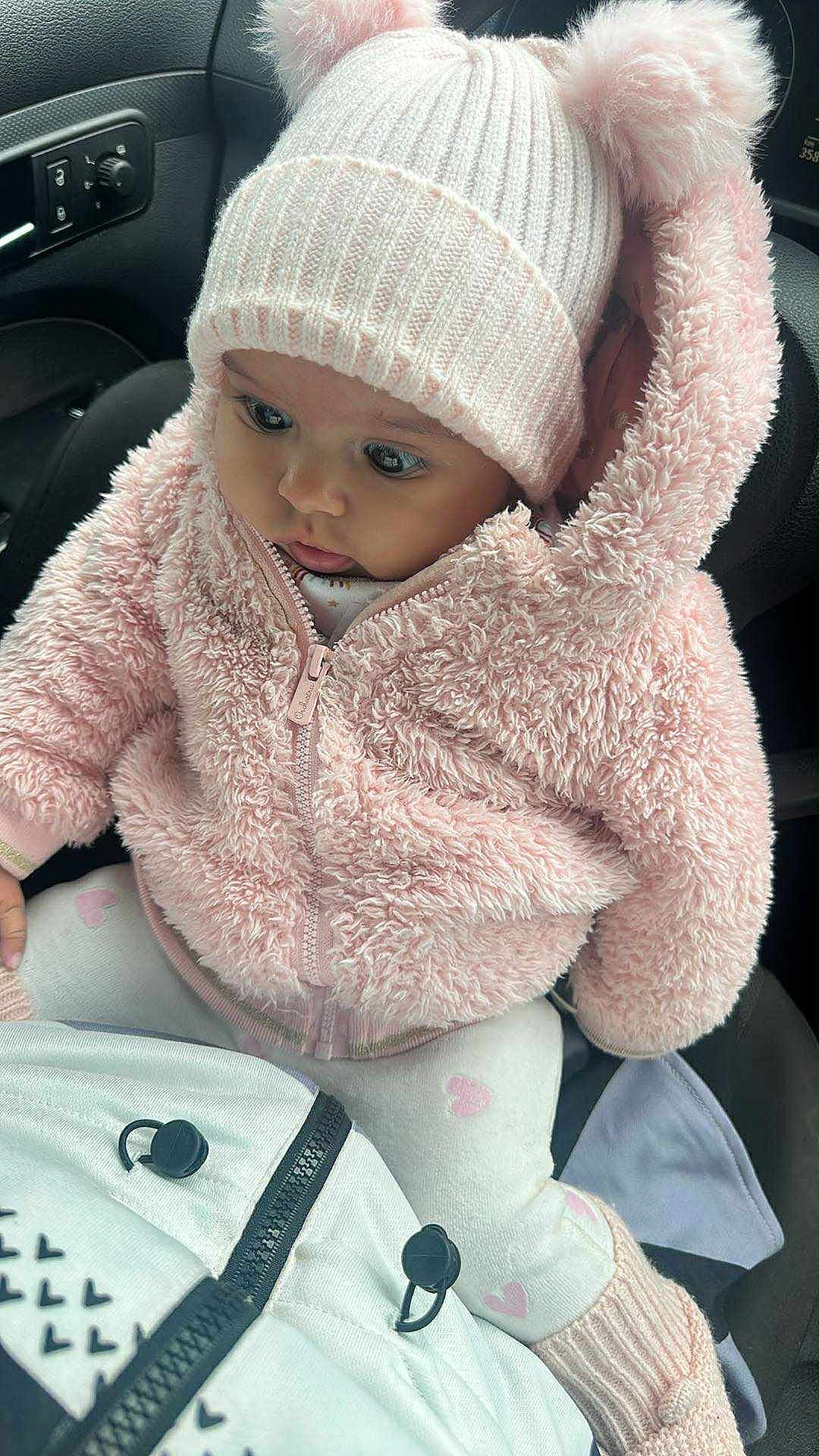 Maïssoum participe au concours pour gagner de l'argent avec cette photo : baby, child, pink_jacket, knit_hat, bear_ears, car_seat, curious, cute, warm_clothing, cozy, pastel_colors, infant, winter_wear, soft_texture, hooded_jacket, sitting, closeup, adorable, indoor, portrait
