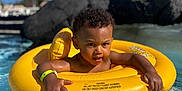 Kaïs participe au concours pour gagner de l'argent avec cette photo : toddler, child, pool, water, inflatable_ring, yellow, floating, sunny, outdoor, summer, curly_hair, wristband, swimming, playful, baby, fun, vacation, leisure, sunlight, relaxation