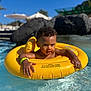 toddler, child, pool, water, inflatable_ring, yellow, floating, sunny, outdoor, summer, curly_hair, wristband, swimming, playful, baby, fun, vacation, leisure, sunlight, relaxation