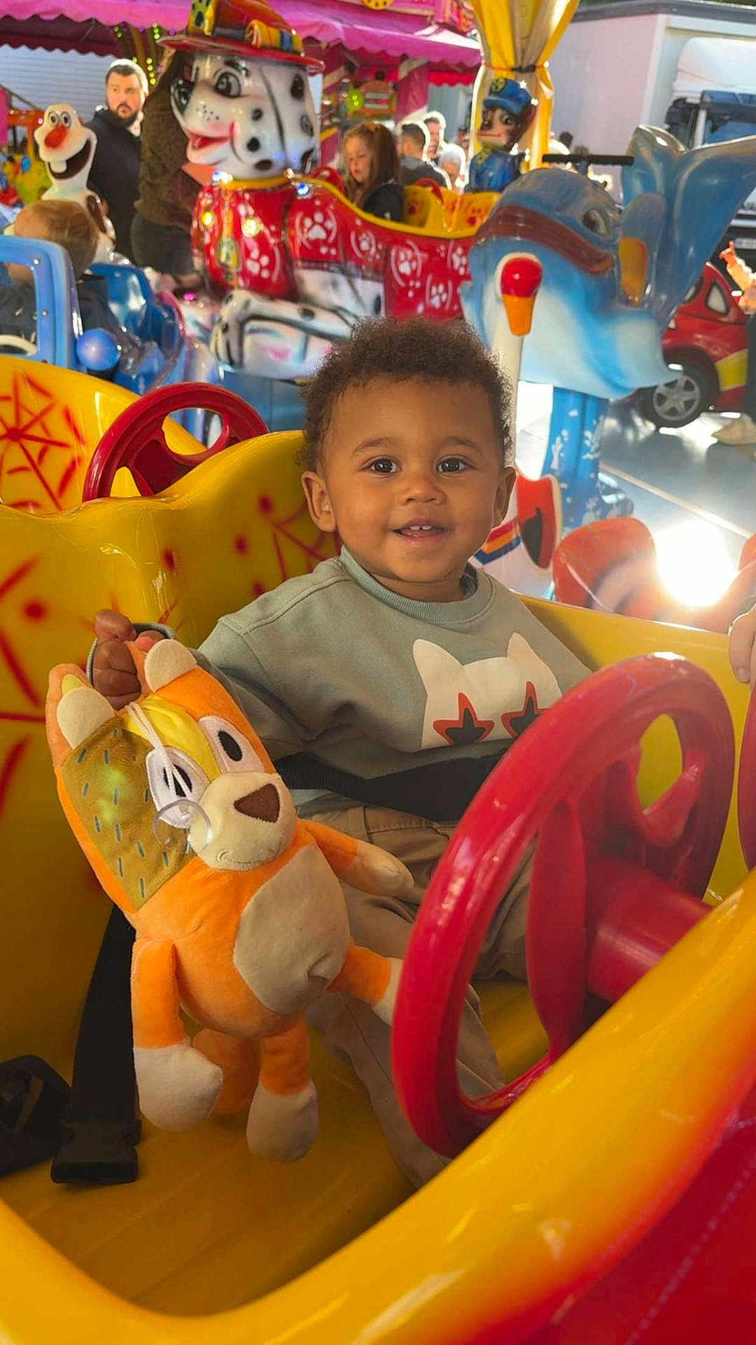 Kaïs a rejoint le concours — aidez-le/la à gagner de superbes lots ! toddler, child, amusement_park, ride, toy, plush, smiling, yellow, red, seatbelt, indoor, fun, happy, person, face, clothing, playful, colorful, carnival, entertainment