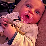 June a rejoint le concours — aidez-le/la à gagner de superbes lots ! arm, baby, candid, closeup, clothing, curious, expression, face, fingers, hand, holding, indoor, infant, pacifier, person, portrait, skin, sleepwear, toy, warmth